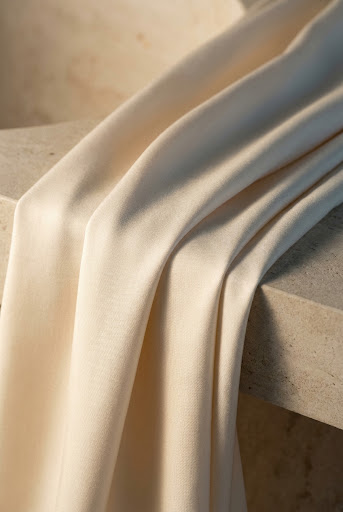 Cream TENCEL Lyocell fabric falling in fluid folds over a warm stone surface